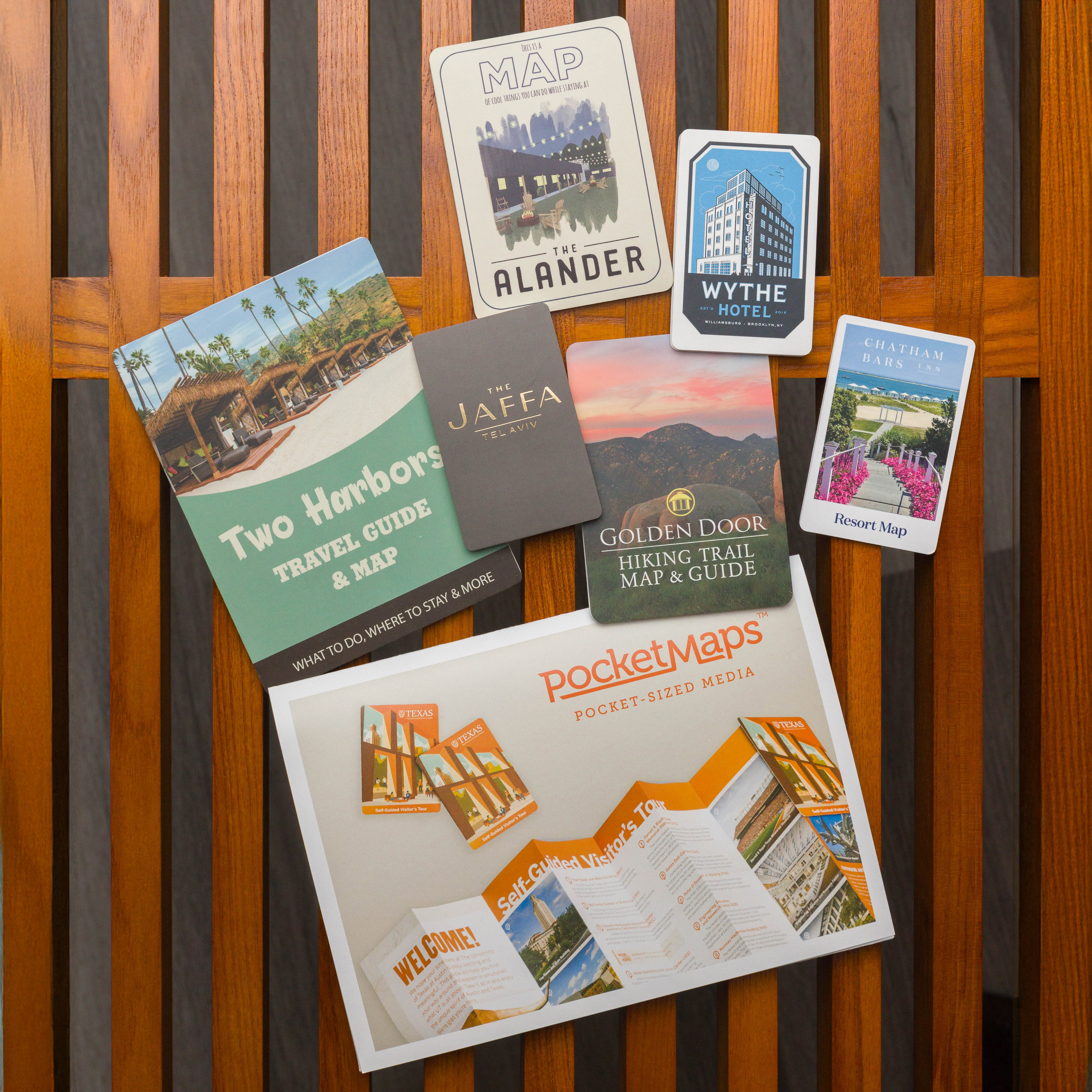 A collection of PocketMaps travel guides and hotel maps displayed on a wooden surface, showcasing compact and visually appealing designs for destinations, resorts, and hiking trails